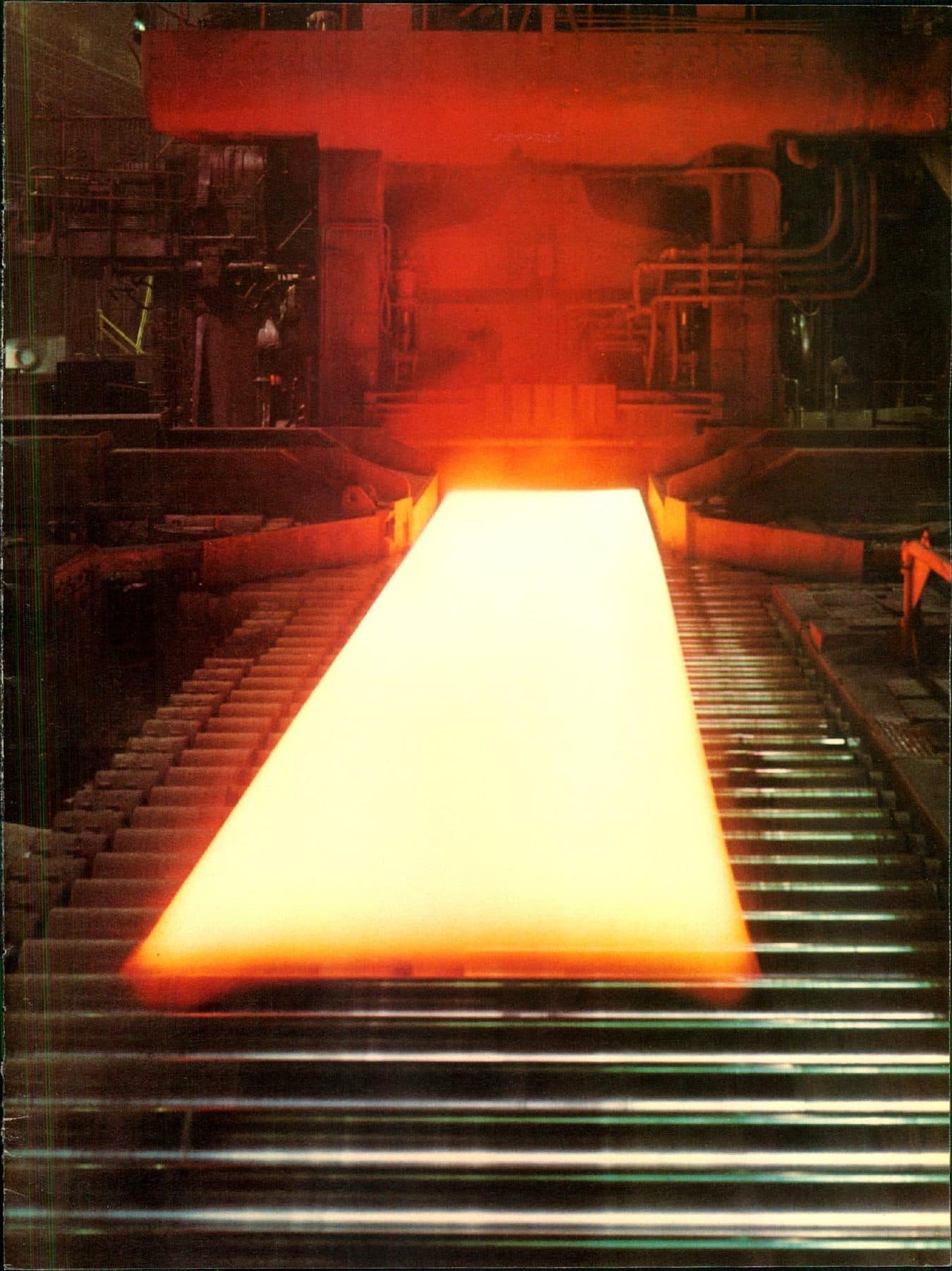 A white-hot slab racing down the mill rollers.