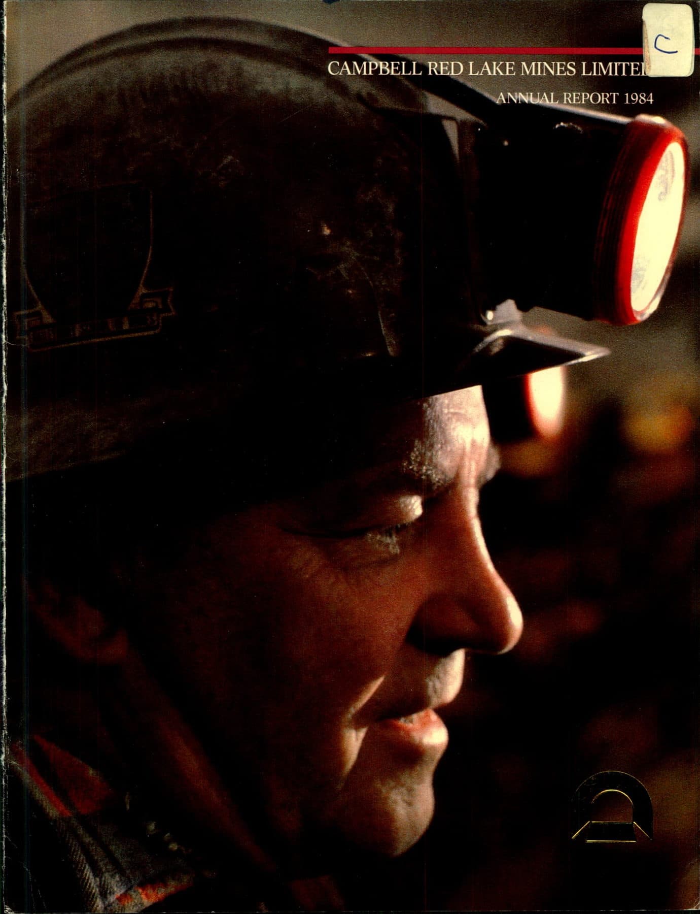 A miner in profile, hard hat and lit headlamp throwing a red glow on his face.