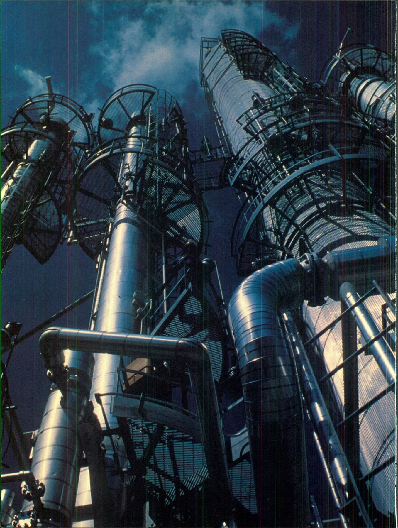 Low-angle view of vertical process towers, clad pipe, and grated platforms against a dark sky.